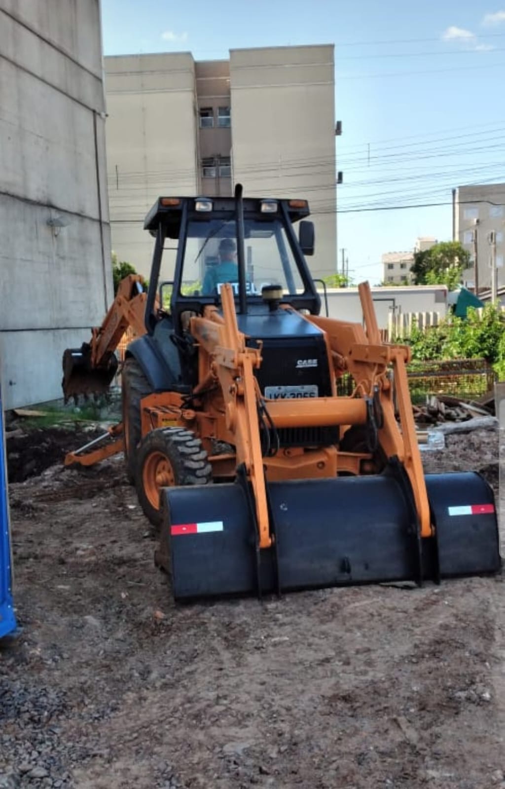 Retroescavadeira com rolo compactador em terreno urbano